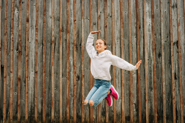 Szabadtéri portré boldog fiatal lány szürke pulóver, pózol a barna háttér, ugrás fel, divat a gyermekek számára - Fotó, kép