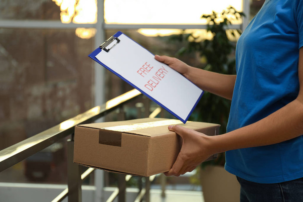 Courier with clipboard holding parcel indoors, closeup - Fotó, kép