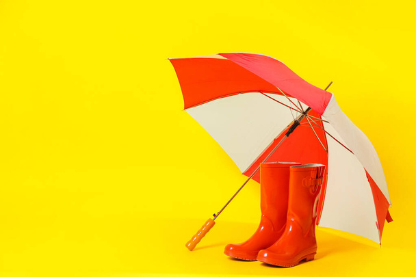 Colorful umbrella and red rubber boots on light yellow background. Space for text - 写真・画像