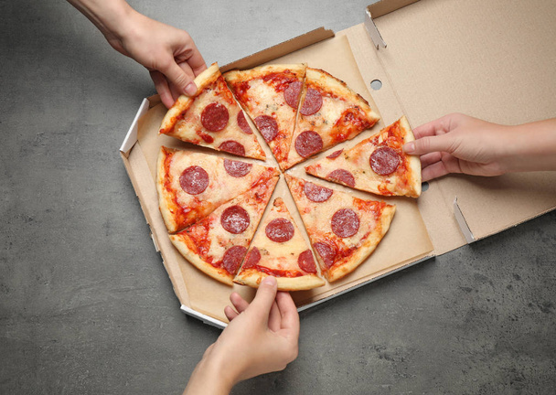 People taking slices of tasty pepperoni pizza at grey table, top view - Fotoğraf, Görsel