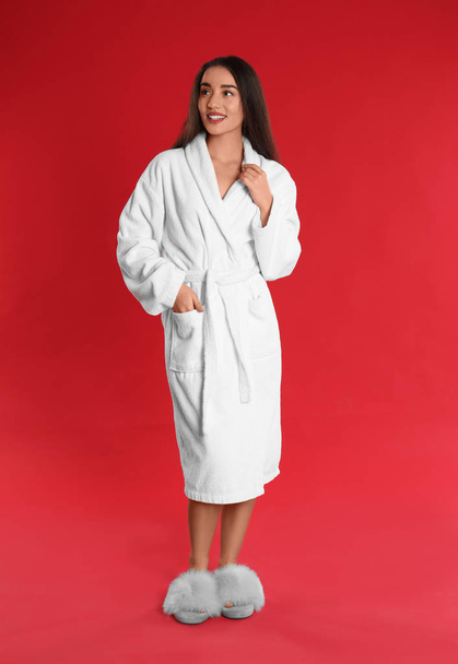 Beautiful young woman in bathrobe on red background - Foto, afbeelding