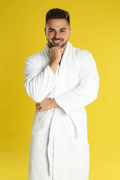 Happy young man in bathrobe on yellow background - Foto, Imagen