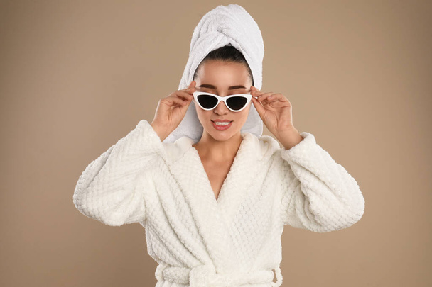 Young woman in bathrobe and sunglasses on brown background - Φωτογραφία, εικόνα