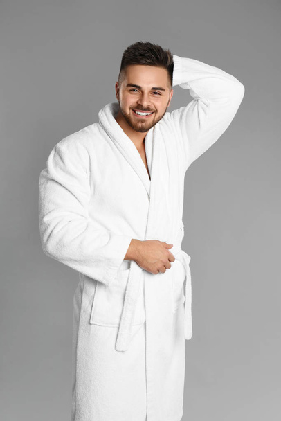 Happy young man in bathrobe on grey background - 写真・画像