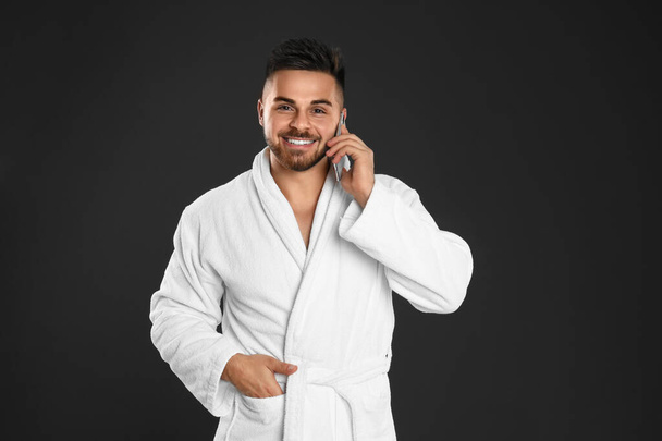 Young man in bathrobe talking on mobile phone against black back - Photo, image