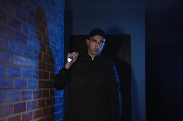 Male security guard with flashlight in dark corridor - Foto, afbeelding