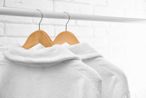 Fresh bathrobes hanging on rack near white brick wall - Φωτογραφία, εικόνα