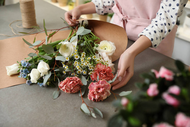 Florist making bouquet with fresh flowers at table, closeup - 写真・画像