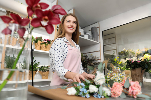 Florist making bouquet with fresh flowers at table in shop - Фото, зображення