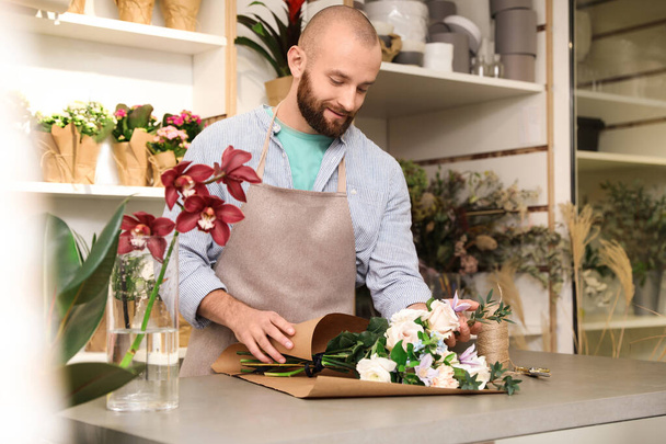 Florist making bouquet with fresh flowers at table in shop - Photo, Image
