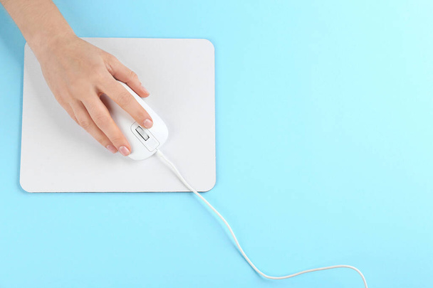 Woman with modern wired optical mouse and pad on light blue background, top view. Space for text - Photo, Image
