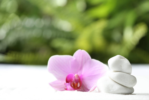 Stapel weißer Steine und schöne Blumen auf Sand vor verschwommenem grünen Hintergrund. Zen, Meditation, Harmonie - Foto, Bild
