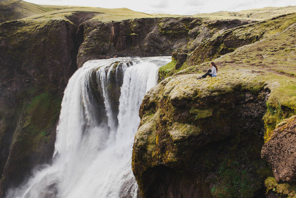 Žena sedí na okraji s úchvatným výhledem na Fagrifoss waterf - Fotografie, Obrázek