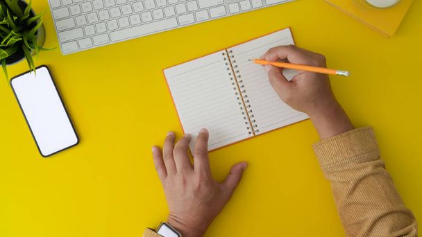 Top view of man working on his project by writing on notebook in trendy workplace  - 写真・画像