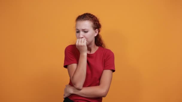 Pelokas nuori nainen punaisessa paidassa pitää kädestä suuhun
 - Materiaali, video