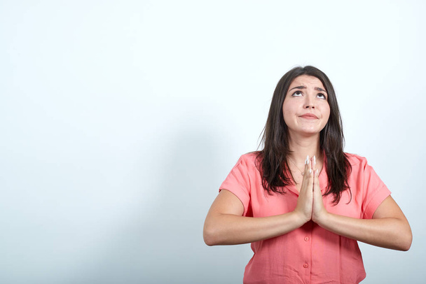 Ειρηνική νεαρή γυναίκα με ροζ πουκάμισο κρατώντας το χέρι μαζί, προσεύχεται - Φωτογραφία, εικόνα