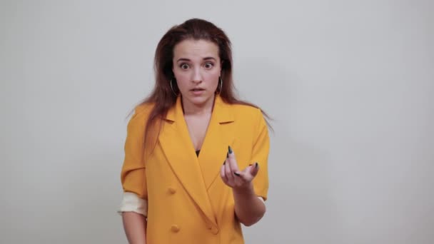Mujer joven asustada en chaqueta amarilla manteniendo la mano en la boca mordiéndose las uñas
 - Metraje, vídeo