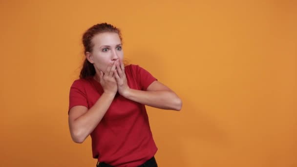 Jovencita asustada en camisa roja cubriendo la boca con la mano, mirando asustada
 - Metraje, vídeo