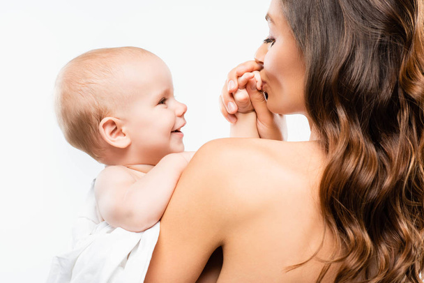 portrait of naked mother kissing hand of baby boy, isolated on white - Zdjęcie, obraz