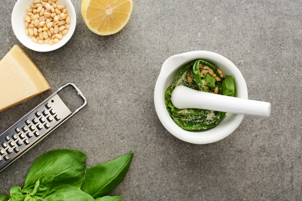 top view of pesto sauce raw ingredients, grater and pounder on grey surface - Zdjęcie, obraz