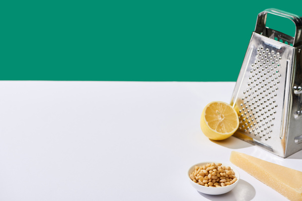 лимон, пармезан, кедровые орехи и терка на белом столе изолированы на зеленый
 - Фото, изображение