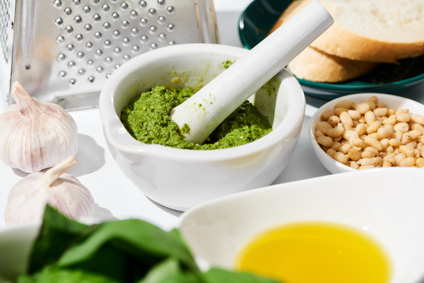 close up view of pesto sauce in pounder near grater, bread and ingredients on white background - Photo, Image
