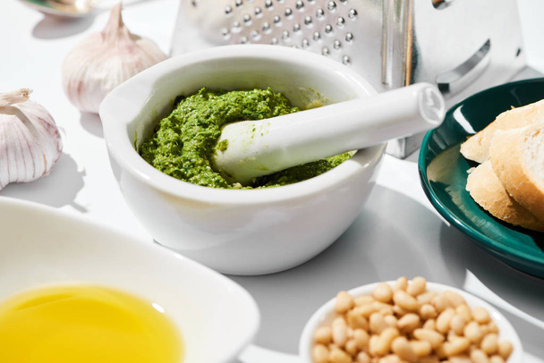 close up view of pesto sauce in pounder near grater, bread and ingredients on white background - Photo, Image