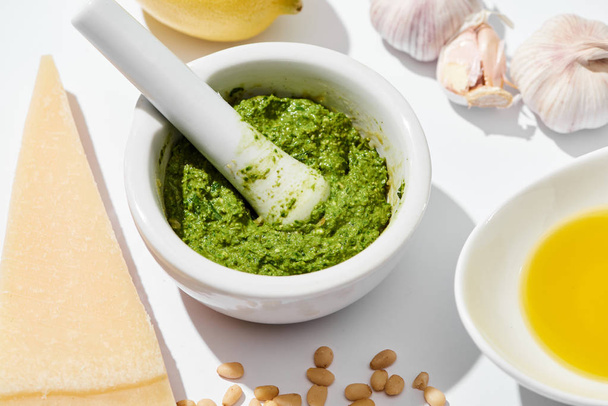 close up view of pesto sauce in pounder near ingredients on white background - Photo, Image
