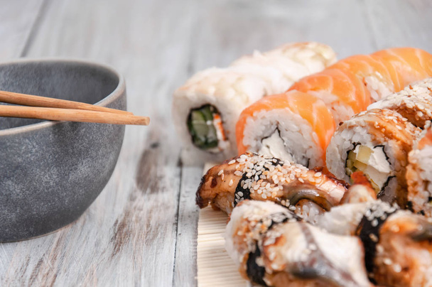 Sushi y salsa de soja en un tazón y palillos de madera en una mesa de madera gris. Comida japonesa. Set de Sushi. Variedad de rollos. Menú. - Foto, imagen
