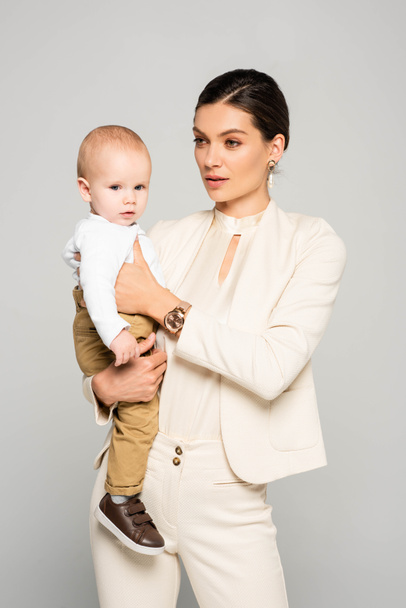 attractive businesswoman with little baby on hands, isolated on grey - Foto, immagini