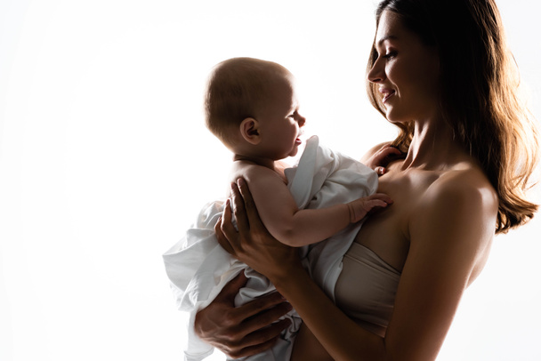 Silhouette einer glücklichen Mutter, die den kleinen Jungen auf Händen hält, isoliert auf Weiß - Foto, Bild