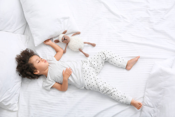 Μικρό Αφροαμερικανό κορίτσι με παιχνίδι που κοιμάται στο κρεβάτι - Φωτογραφία, εικόνα
