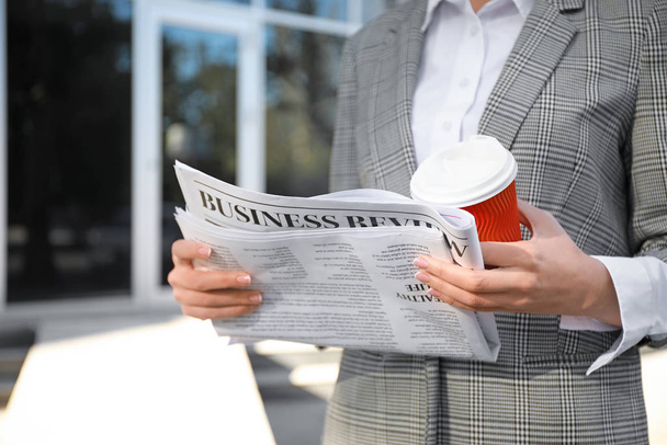 Young businesswoman with newspaper and cup of coffee outdoors - Фото, изображение