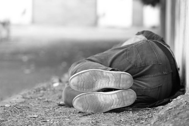 Zwart-wit foto van arme dakloze man slapen op de grond buiten - Foto, afbeelding