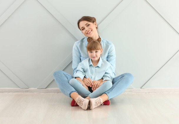 Portrait of happy mother and daughter sitting on floor near wall - Photo, Image