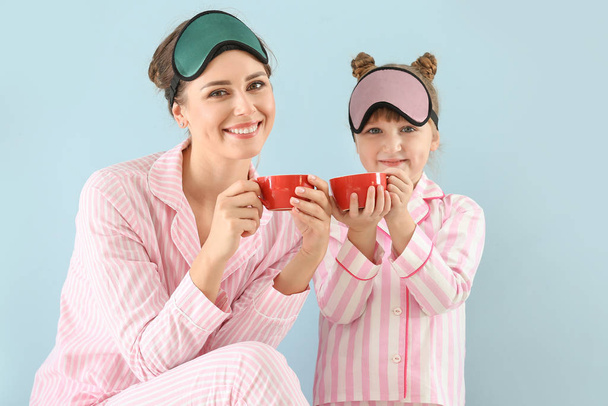 Portret szczęśliwej matki i córki w piżamie i maskach nasennych pijących herbatę na kolorowym tle - Zdjęcie, obraz