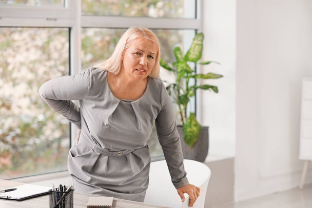 Mature woman suffering from back pain in office - Photo, Image