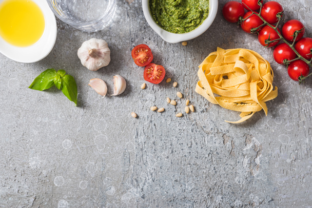top view of raw Pappardelle near tomatoes, garlic, basil, pine nuts, olive oil, water and pesto sauce on grey surface - Fotoğraf, Görsel