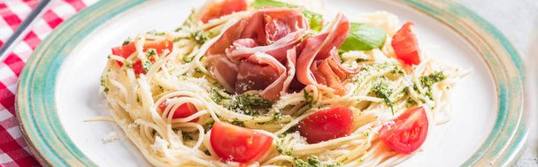Pappardelle with tomatoes, basil and prosciutto on grey surface with plaid napkin, panoramic shot - Photo, Image