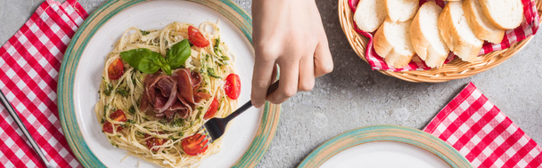 トマトとバジルとプロシュートを添えたパパルデッレを食べる女性のクロップドビュー灰色の表面にバゲットの近く,パノラマショット - 写真・画像