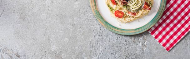 top view of served Pappardelle with tomatoes, basil and prosciutto on plaid napkin on grey surface, panoramic shot - Фото, изображение