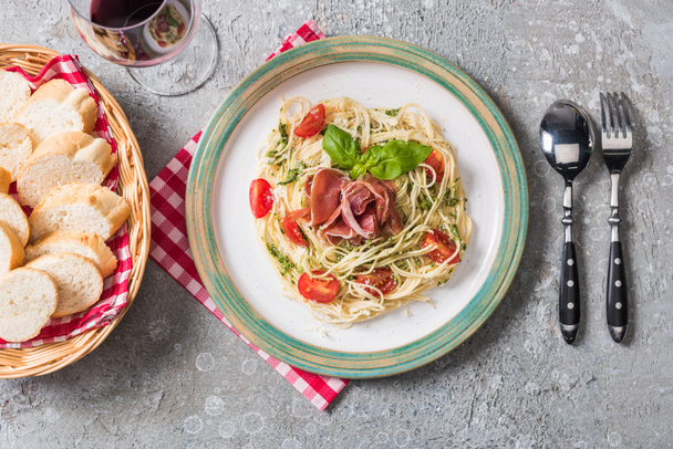 Baget, kırmızı şarap ve gri yüzeye servis edilen domates, fesleğen ve prosciutto ile servis edilen Pappardelle 'in üst görüntüsü - Fotoğraf, Görsel