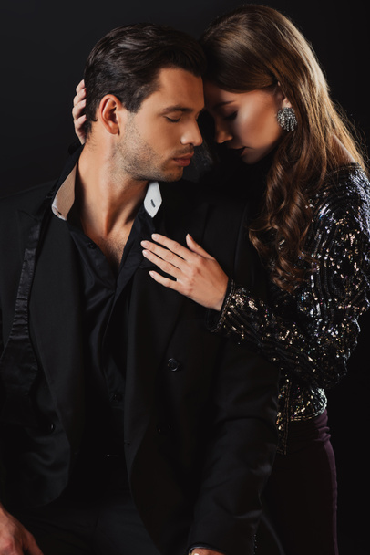 attractive woman hugging handsome man in suit isolated on black - Fotografie, Obrázek