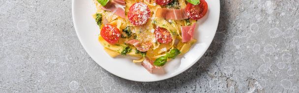 top view of cooked Pappardelle with tomatoes, pesto sauce and prosciutto on grey surface, panoramic shot - Photo, image