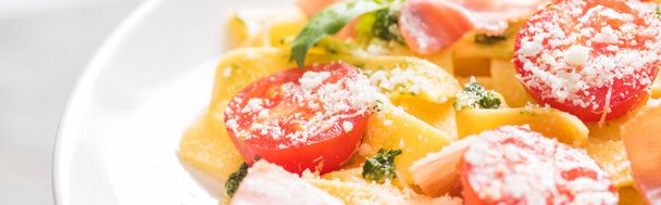 van dichtbij uitzicht op heerlijke Pappardelle met tomaten, Parmezaanse kaas, pestosaus, basilicum en prosciutto - Foto, afbeelding