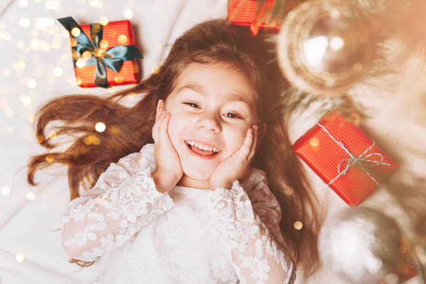 Cute happy little girl Laughing in Christmas atmosphere with gift boxes and magic lights. - Foto, Bild