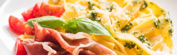 закрыть вид на вкусный Pappardelle с помидорами, пармезан, соус песто, базилик и прошутто, панорамный снимок
 - Фото, изображение