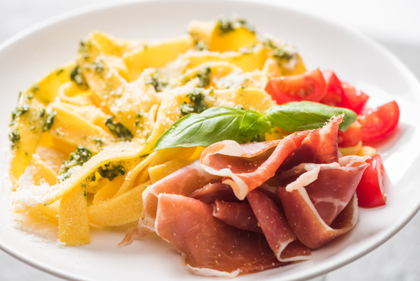 close up view of delicious Pappardelle with tomatoes, Parmesan, pesto sauce, basil and prosciutto - Photo, Image