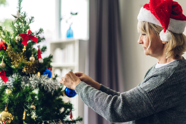Noel Baba şapkalı kadın Noel ağacını süslerken ve gülümserken eğleniyor. - Fotoğraf, Görsel