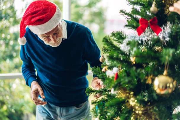Homem sênior relaxante decorando árvore de Natal e sorrindo enquanto
 - Foto, Imagem
